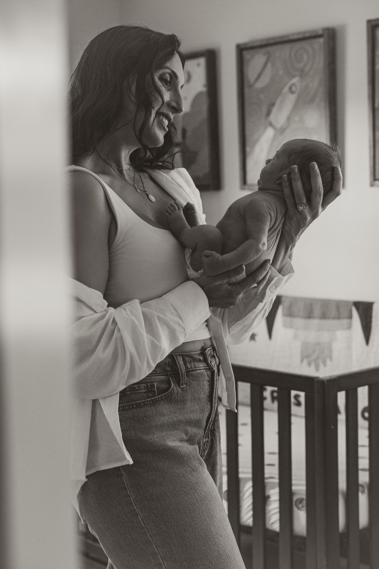 Black and white photo of a smiling mother tenderly holding her newborn baby in a nursery room.
