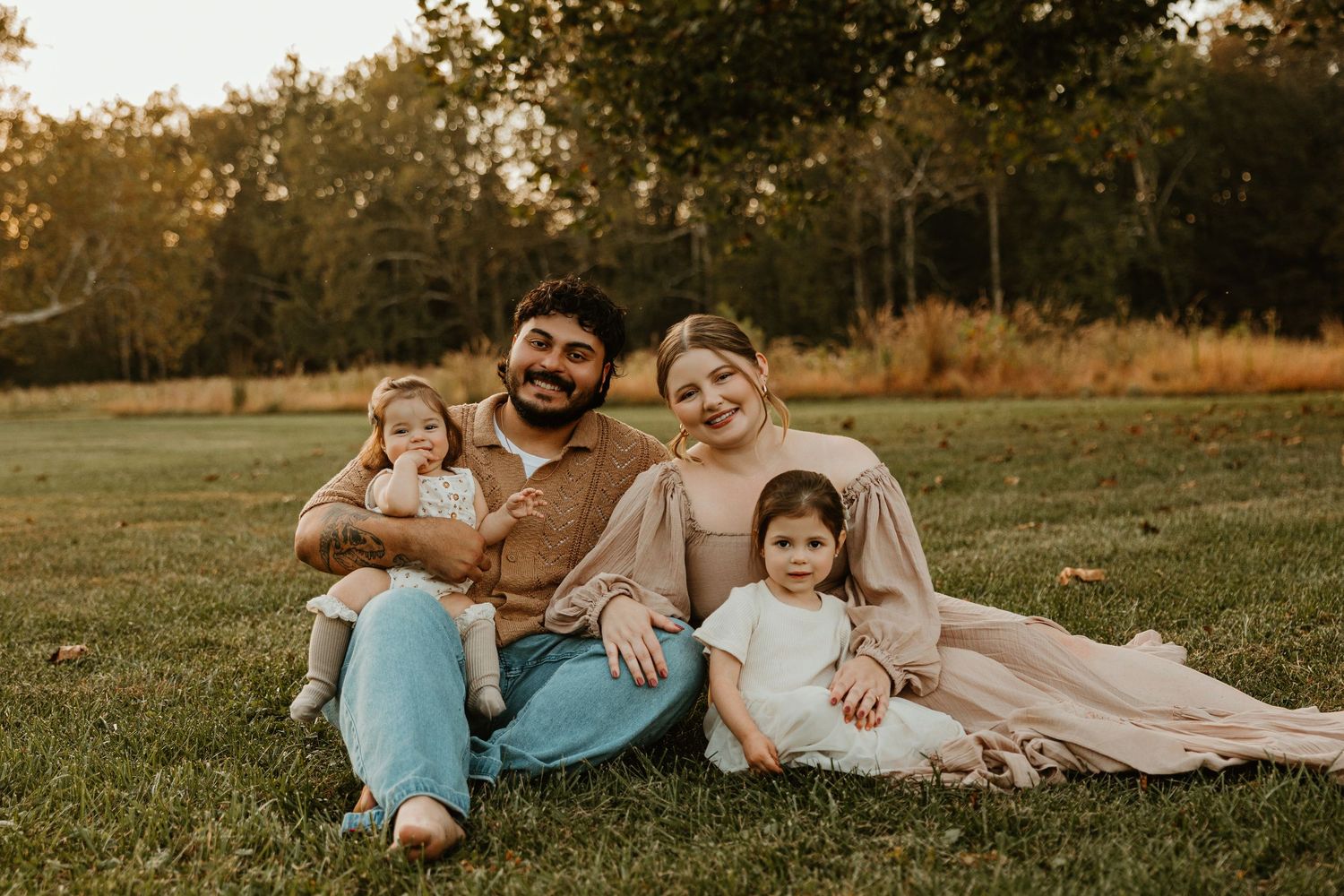 Family relaxes together on grass during golden hour autumn photoshoot.