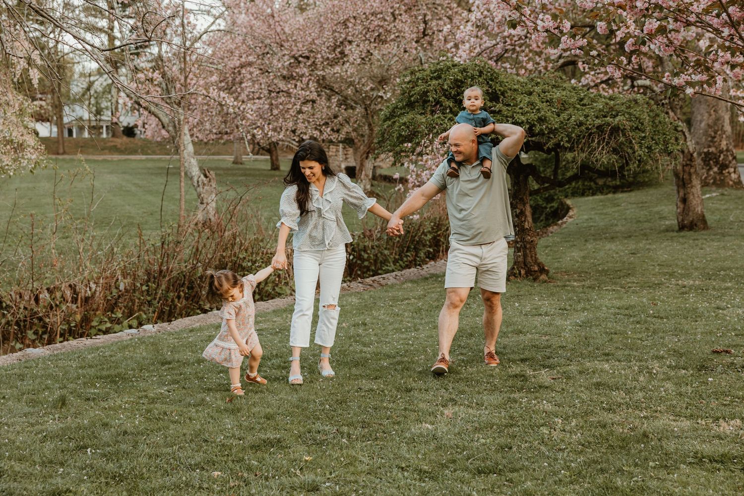 Family of four enjoying a spring day outdoors, with blooming cherry blossom trees in a lush green park.