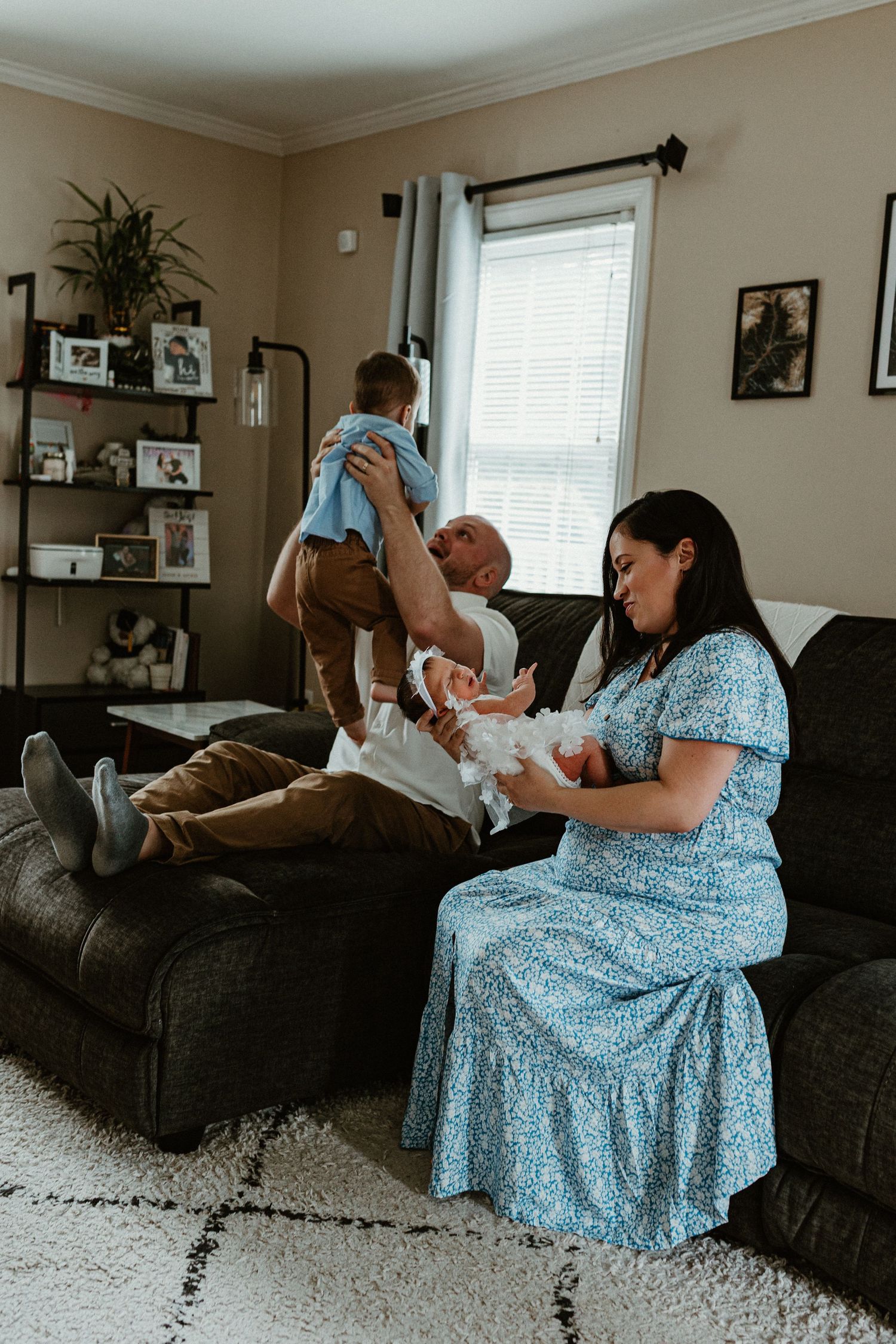 A family shares tender moments together on a gray couch in their living room.