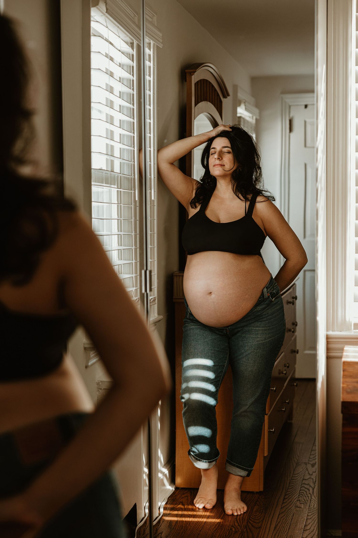 Expectant mother poses by window during intimate indoor maternity session.