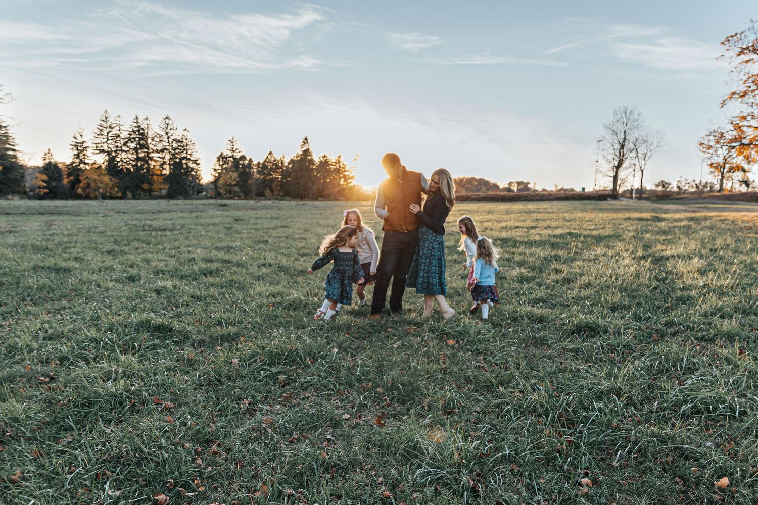 Family enjoying golden hour in a grassy field during autumn sunset.