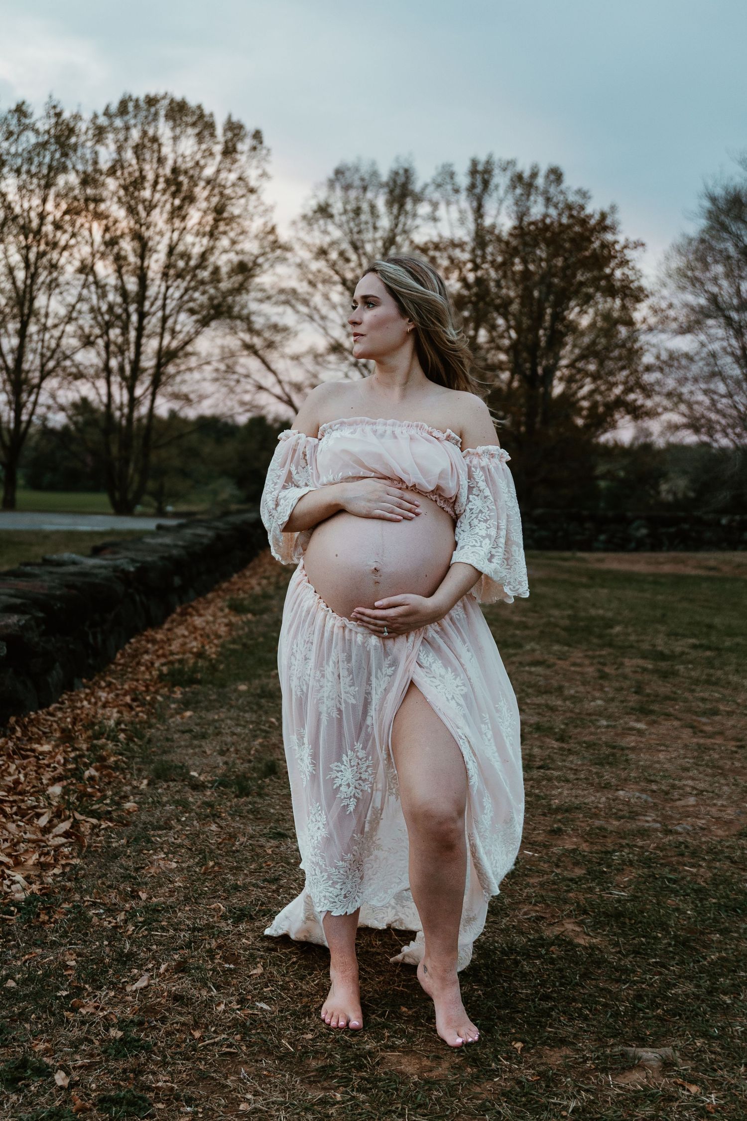 A maternity photoshoot in a white lace dress against a sunset backdrop.