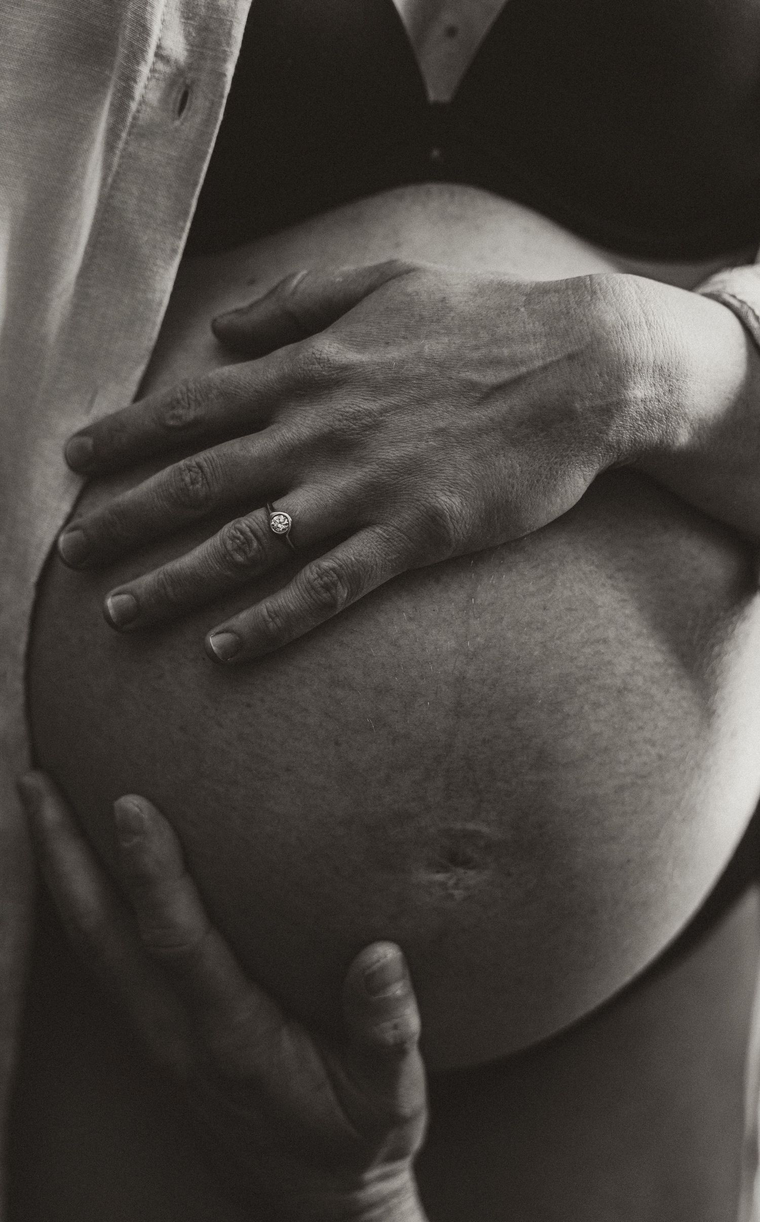 Artistic black and white close-up of pregnant belly with gentle hand placement.