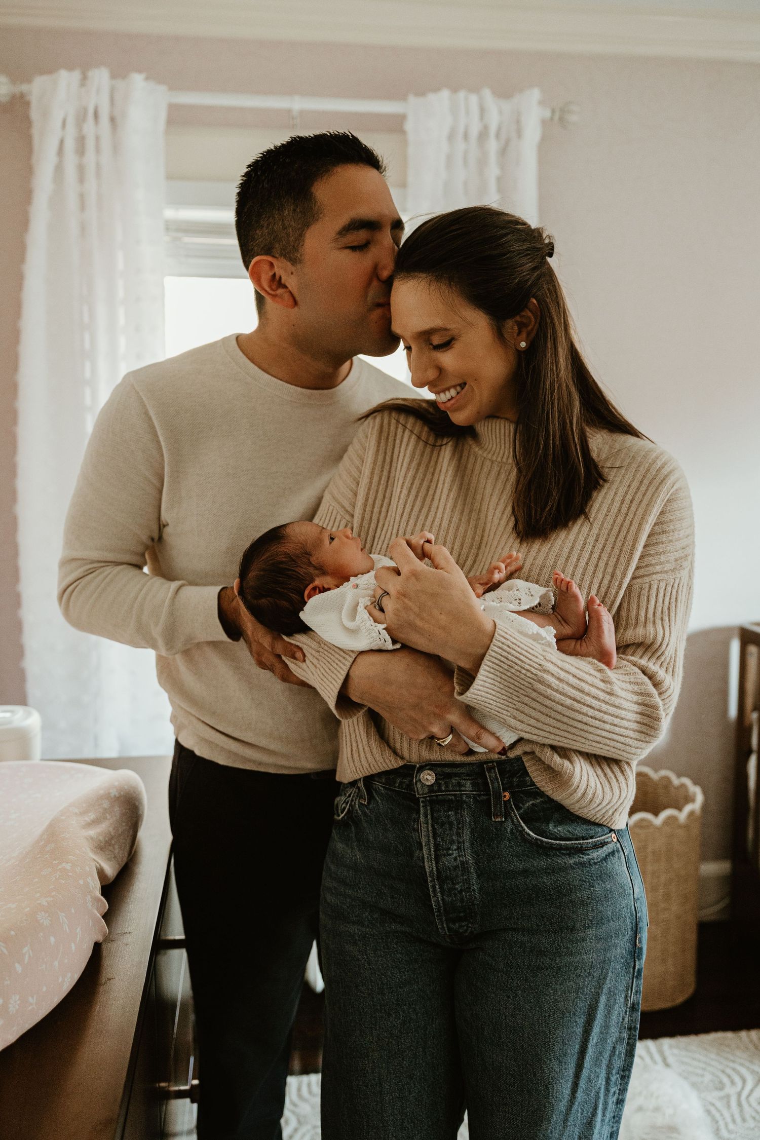 Tender family moment captured in a bright room with white curtains.