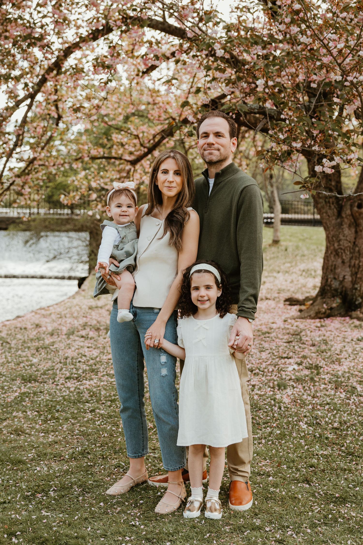 Family of four posing under blooming cherry blossom tree in spring park setting.