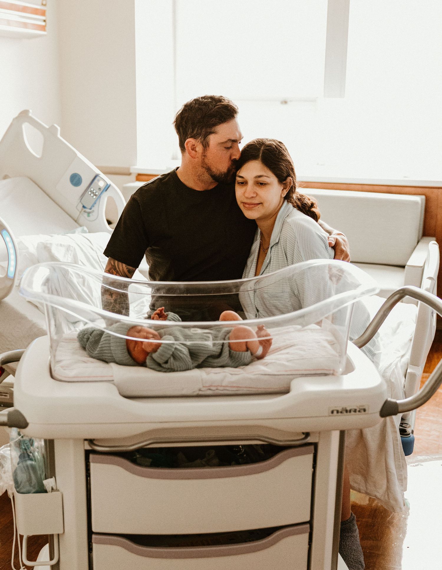 New parents lovingly gaze at their newborn baby in a hospital bassinet after delivery.