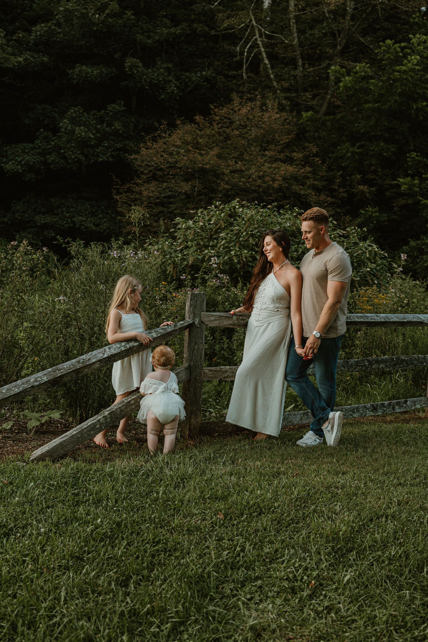 Family of four enjoying a peaceful outdoor moment by a rustic wooden fence surrounded by lush greenery.