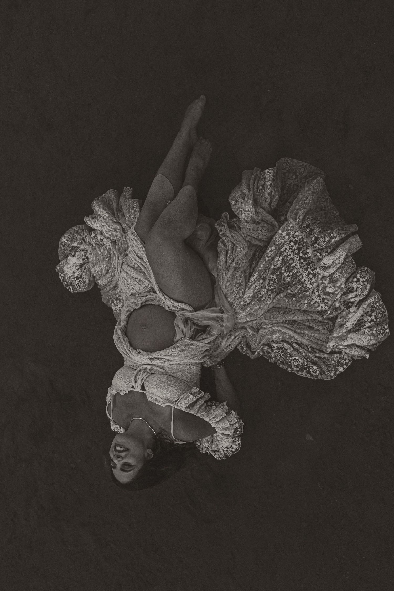 Aerial black and white photo of a dancer in ornate lace costume, gracefully posed against dark background.