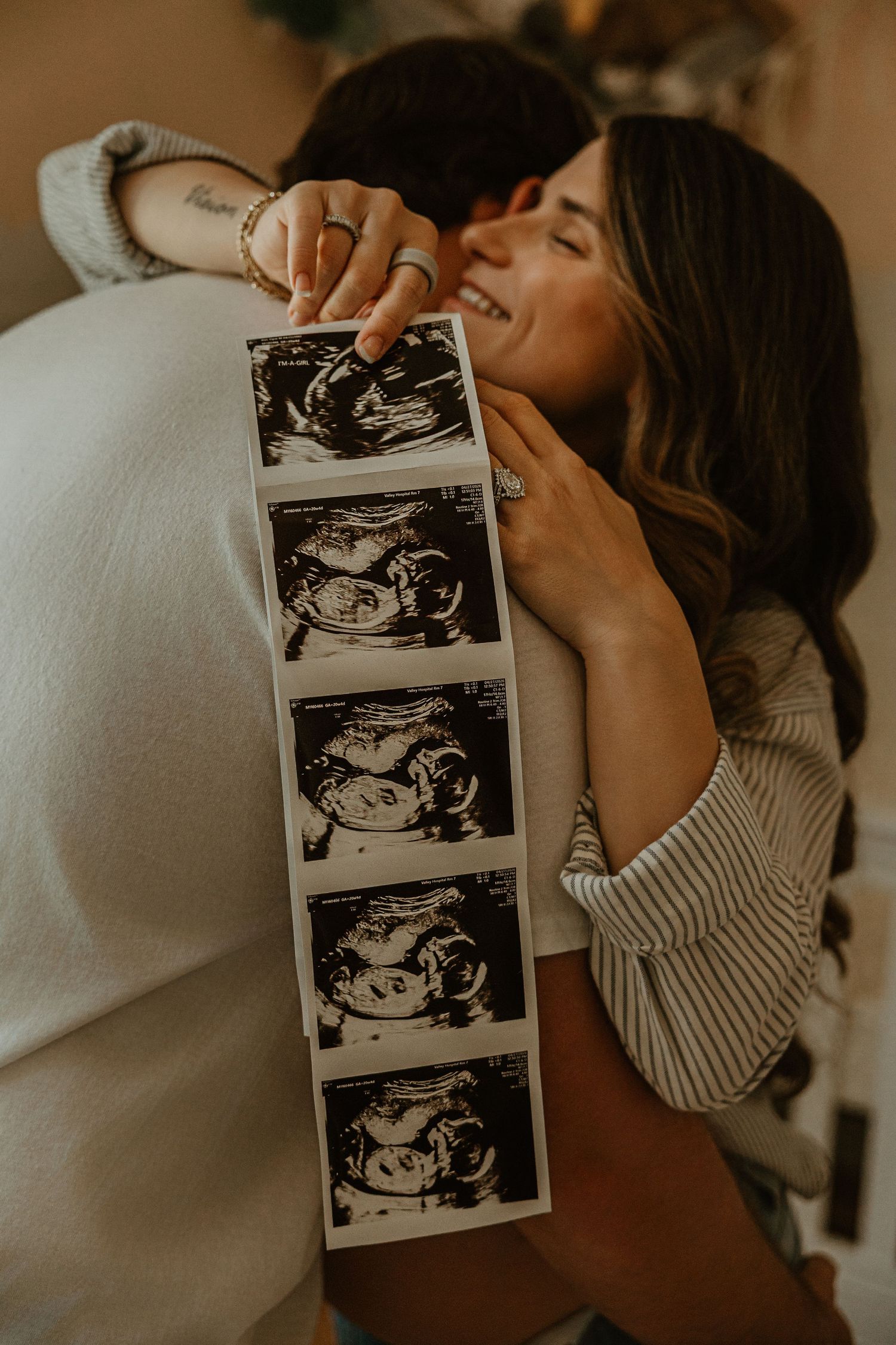 Happy couple embracing and holding ultrasound sonogram photos, celebrating pregnancy announcement together.