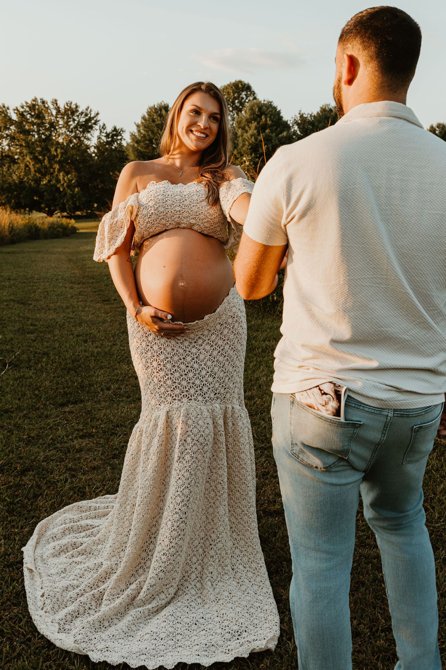 Outdoor maternity photoshoot with couple in casual attire during golden hour.