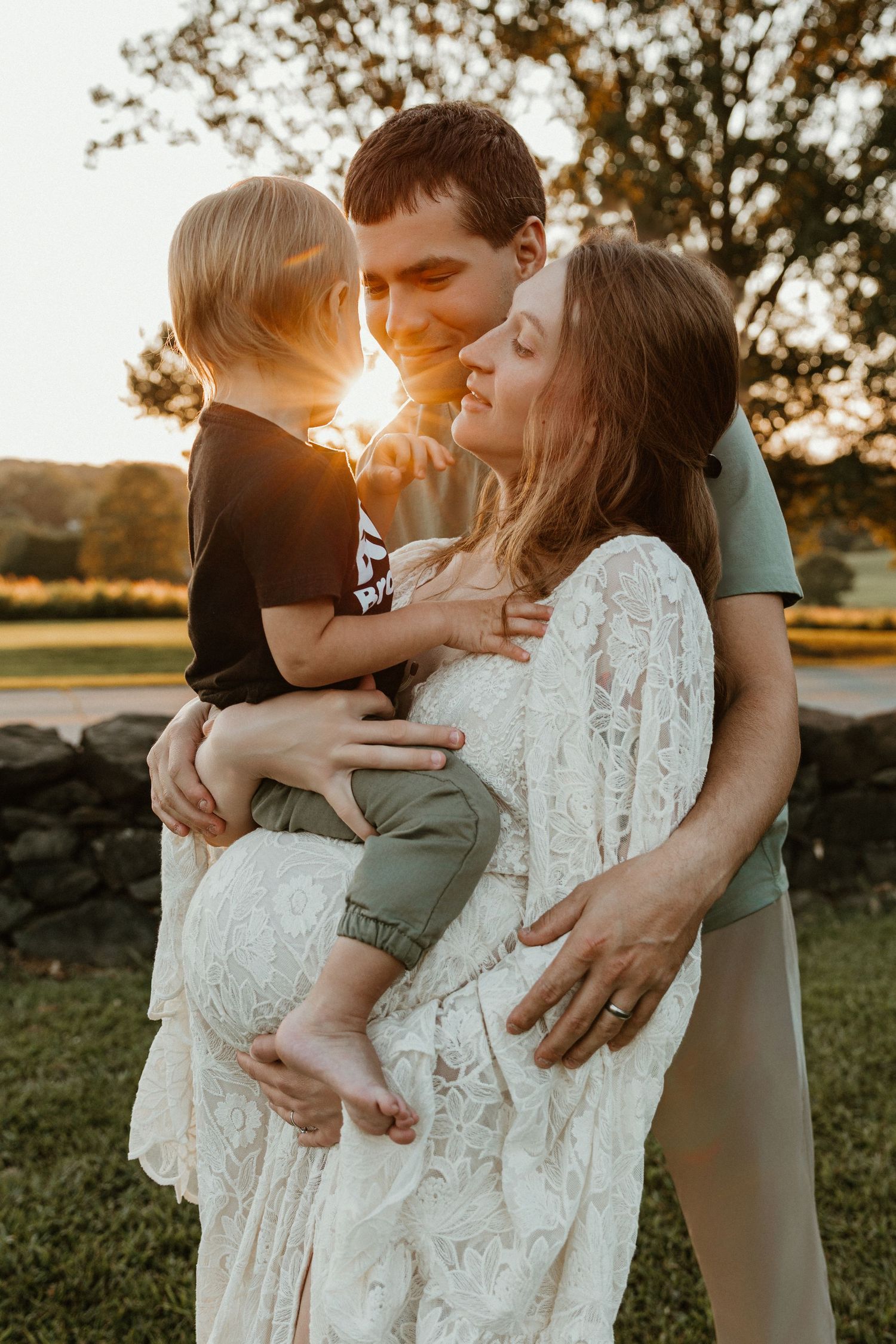 Family maternity photo session at golden hour with a toddler and white lace dress.