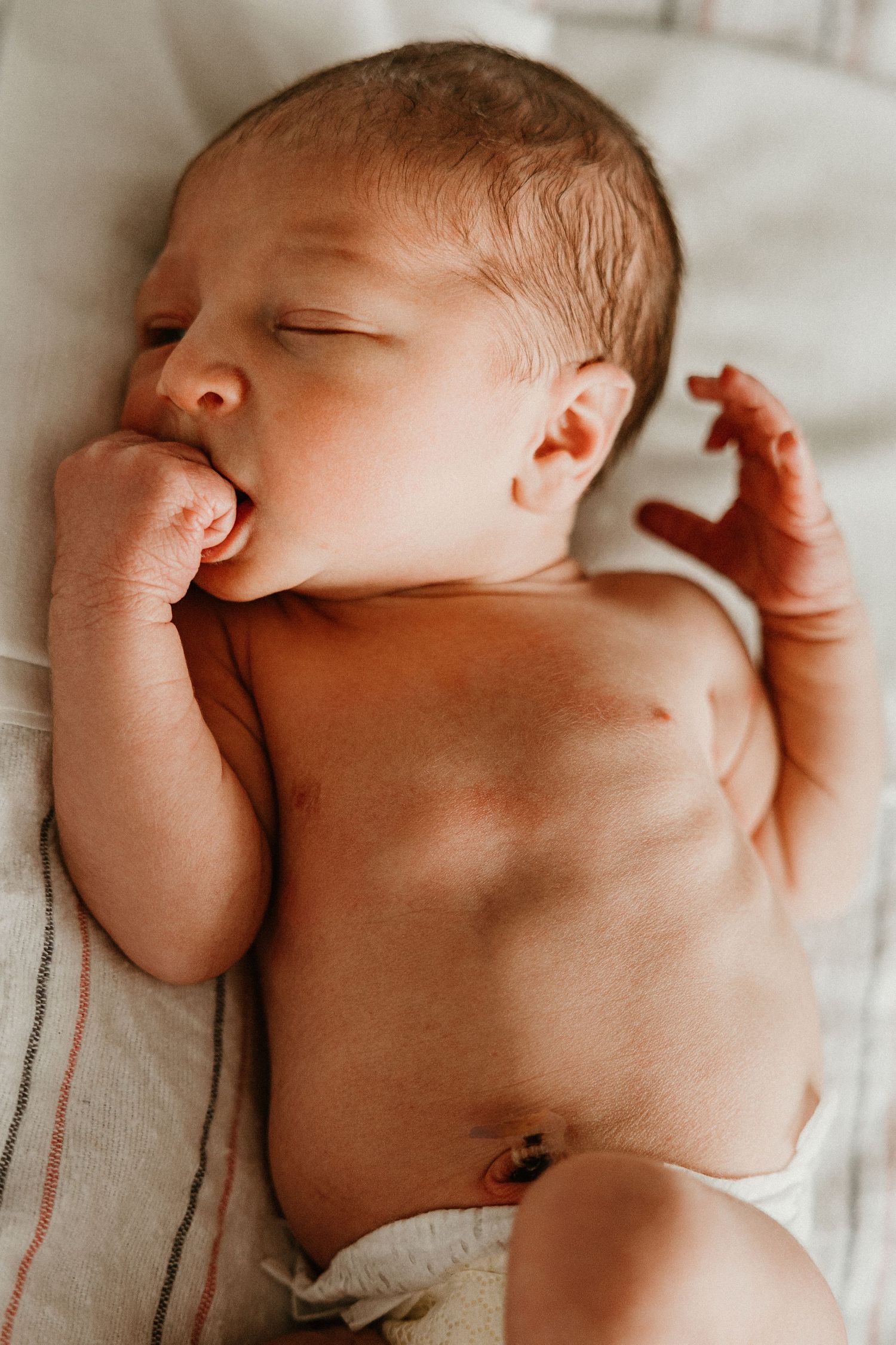 Peaceful newborn baby sleeping on white blanket with fist near mouth in hospital.