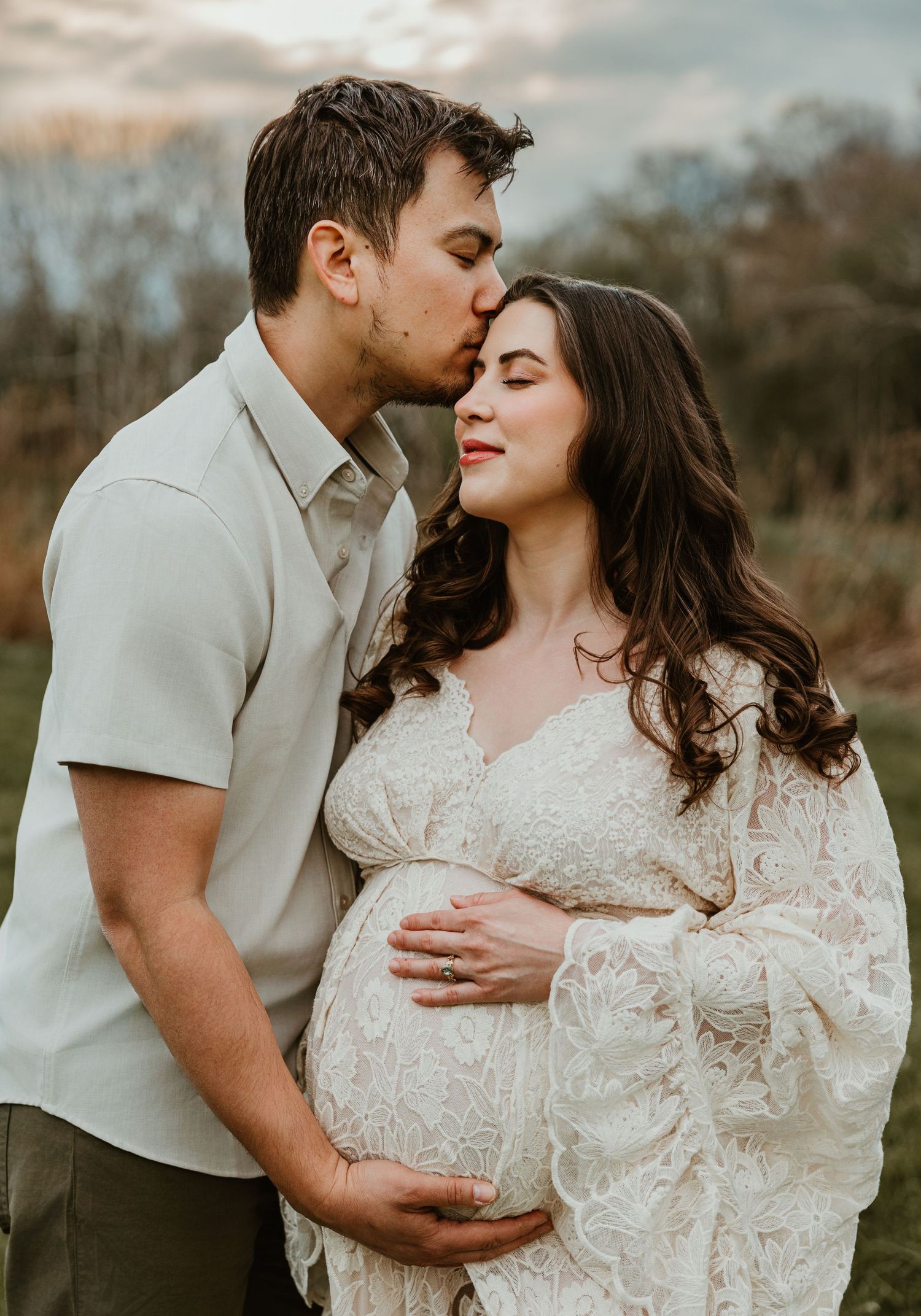 Couple sharing a tender moment during maternity photo shoot outdoors at golden hour.