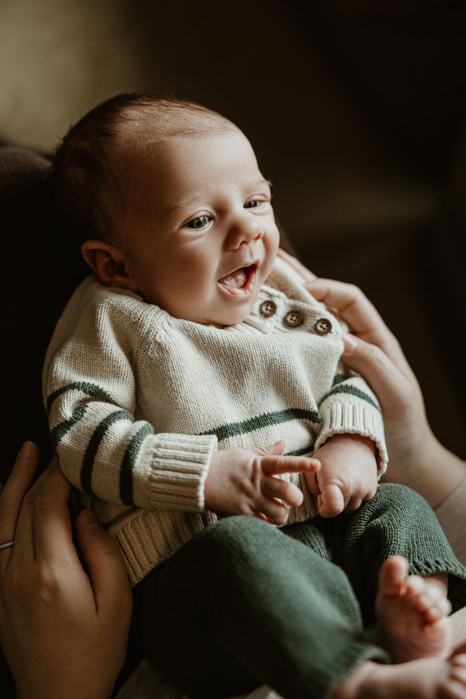 Baby in cozy white knit sweater with buttons rests peacefully in caregiver's hands.