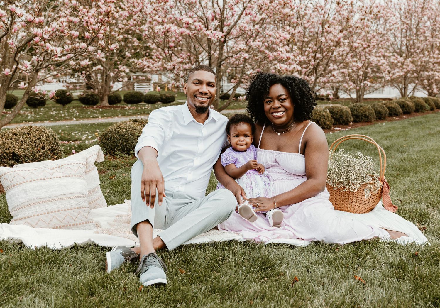 Family having spring picnic under blooming cherry trees with picnic basket on white blanket.