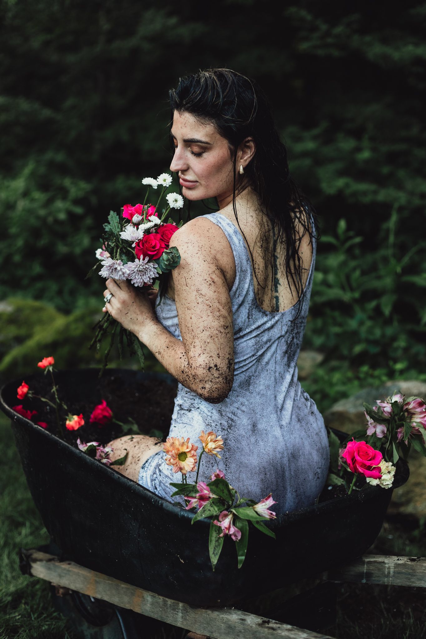 woman in wheelbarrow holding flower, emotional, raining, garden, dramatic, lifestyle, creative photoshoot, themed