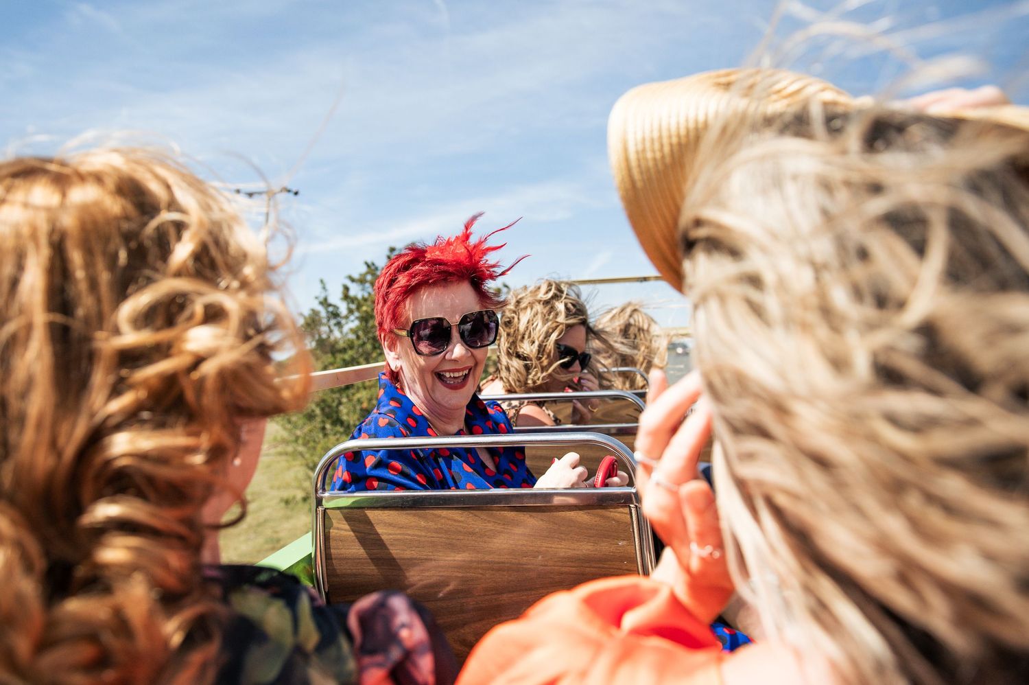 Woman with red hair and sunglasses smiling on a hayride with friends on a sunny day.