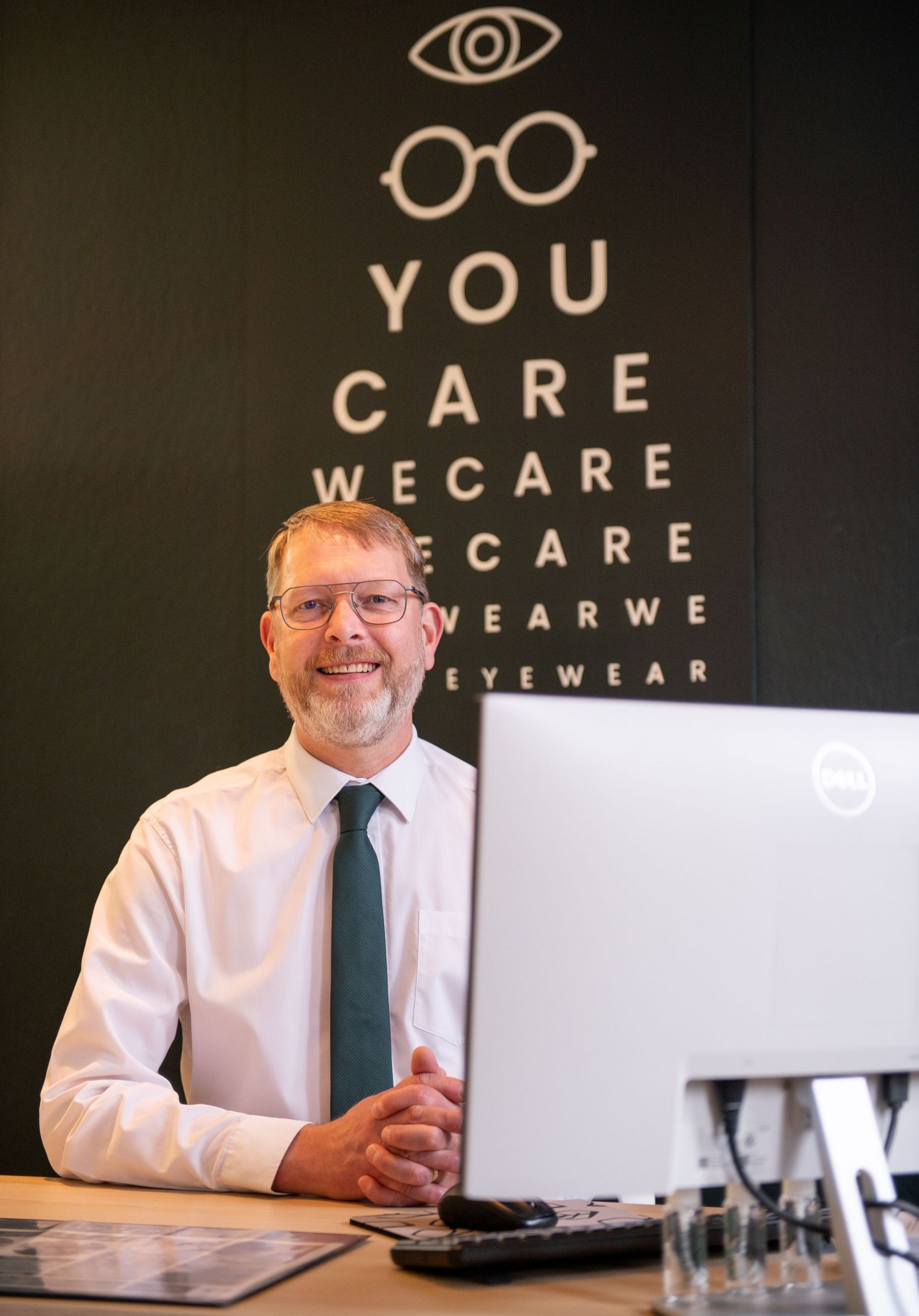 Optometrist at desk with eye chart wall display reading - business photos in Brigg, North Lincolnshire.