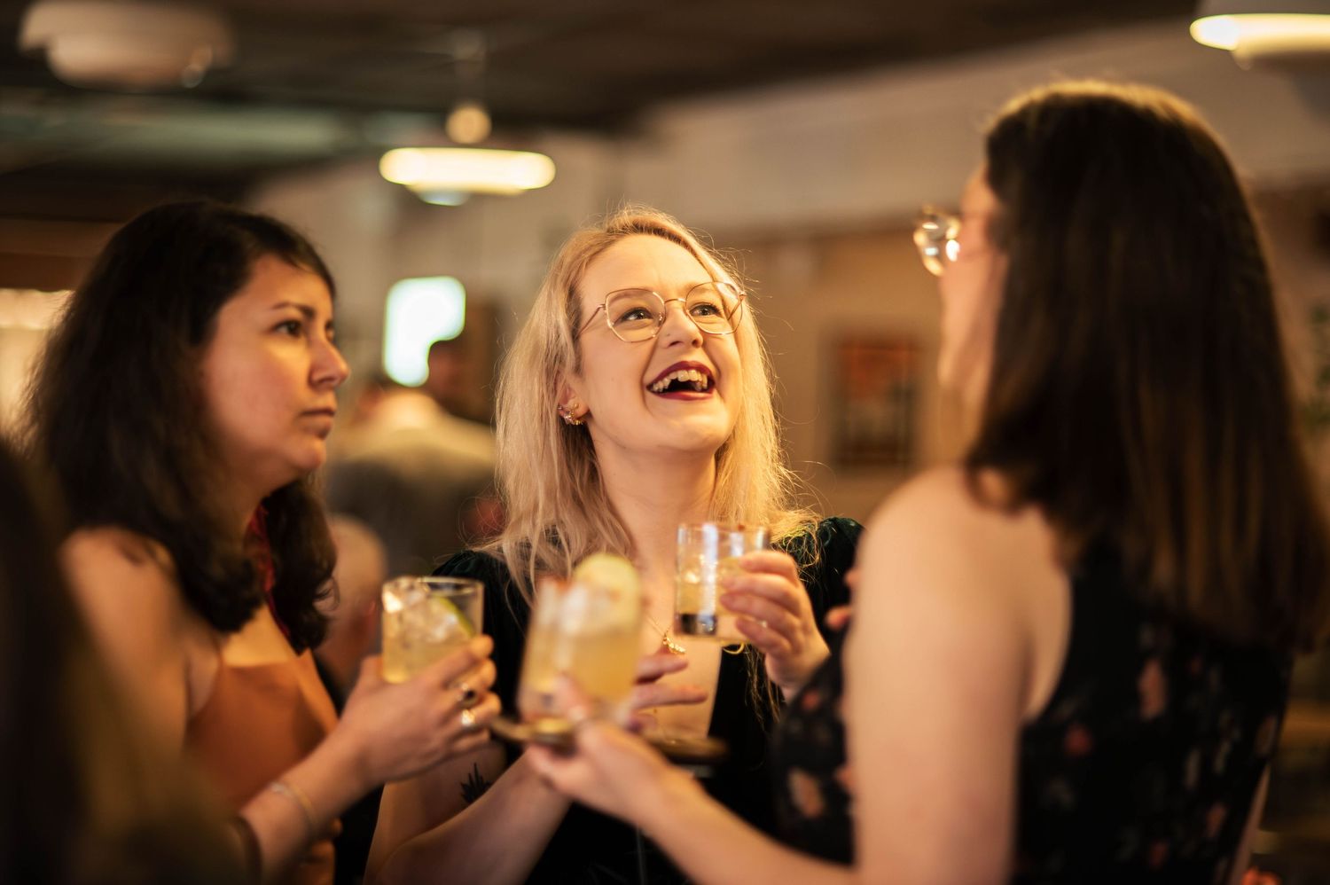 Three women laughing and celebrating with champagne glasses at an elegant indoor party event.