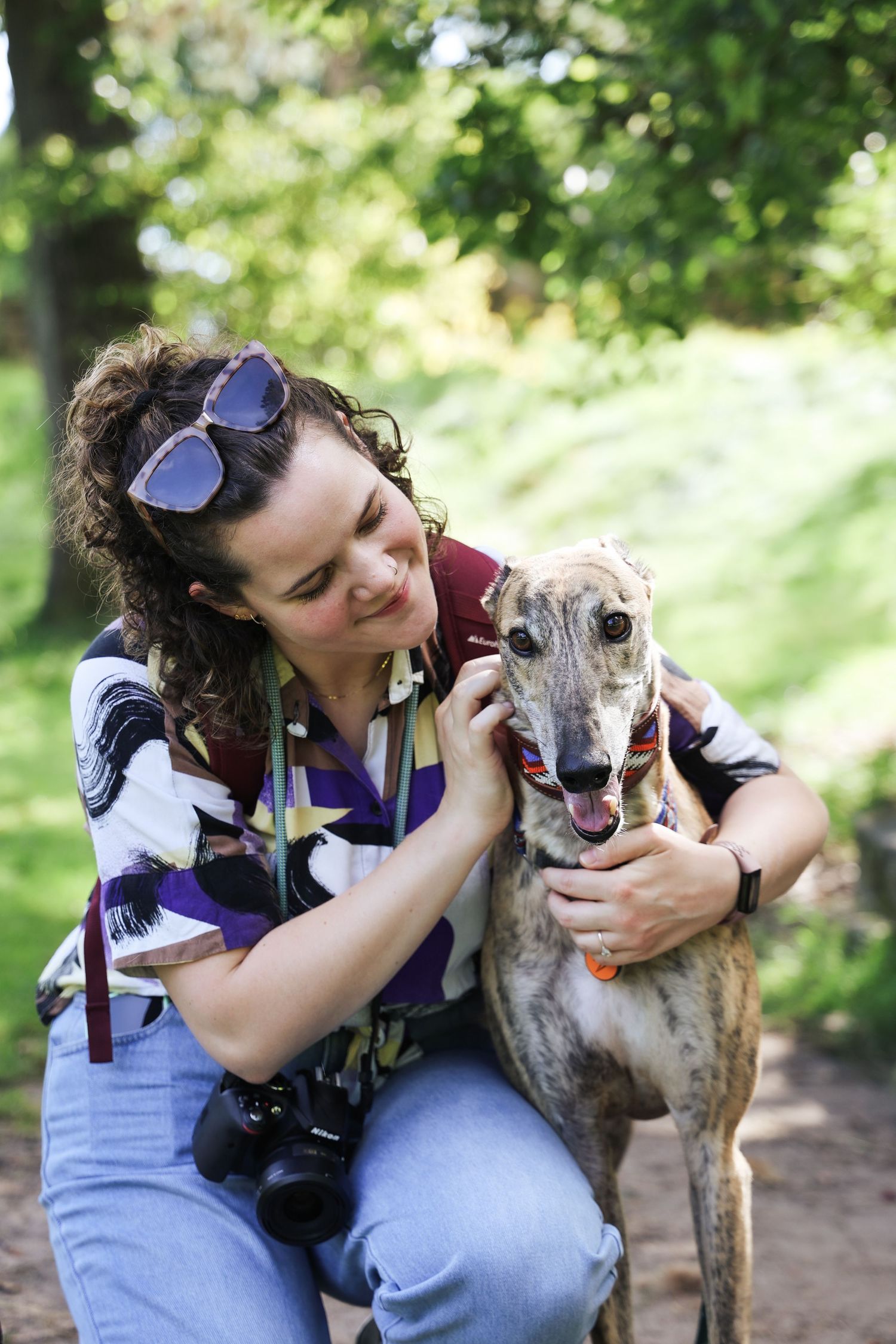 Photographer with camera shows affection to greyhound dog in outdoor setting in Leeds.