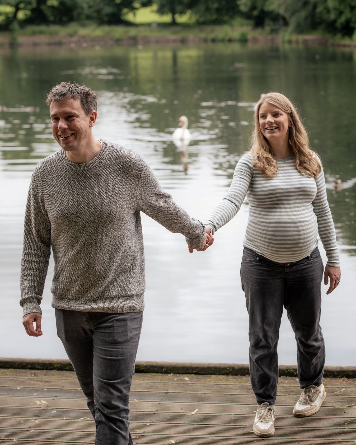 A couple walks together playfully during an outdoor maternity shoot in Leeds, West Yorkshire.