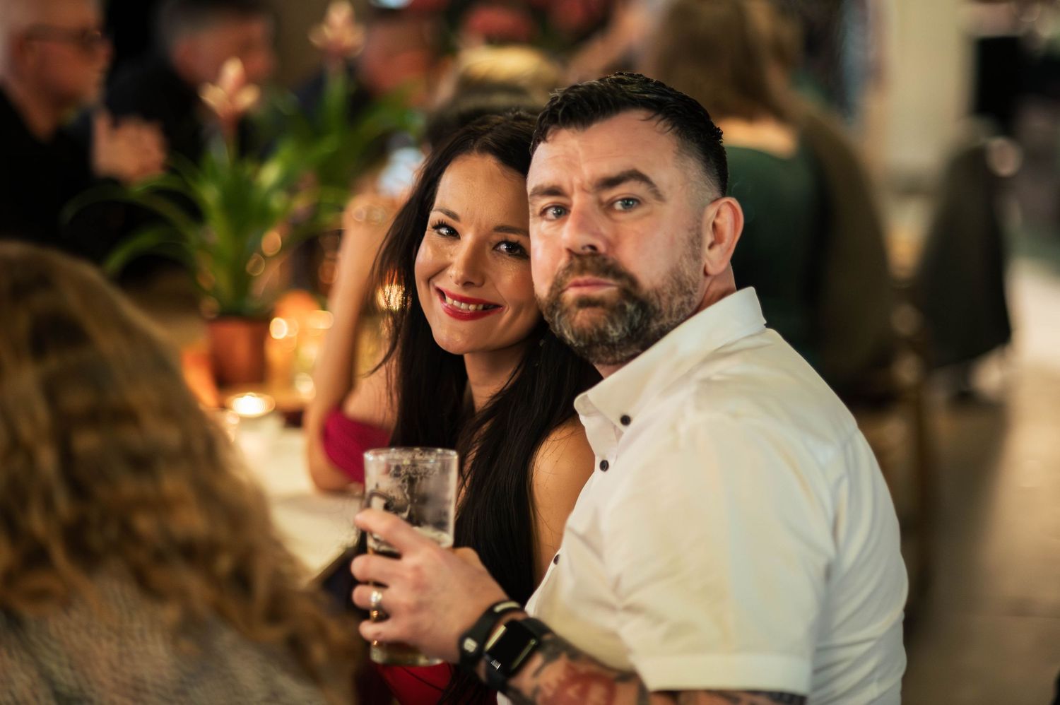 Smiling tattooed couple shares a romantic moment together at a lively wedding reception party.