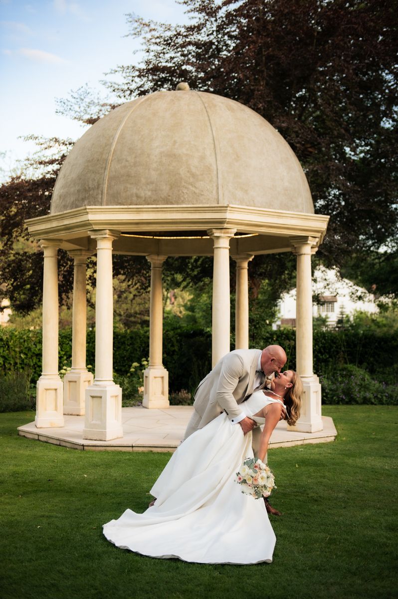 Romantic dip pose of newlyweds under an elegant stone gazebo in a garden setting at Wentbridge House Hotel, Pontefract.