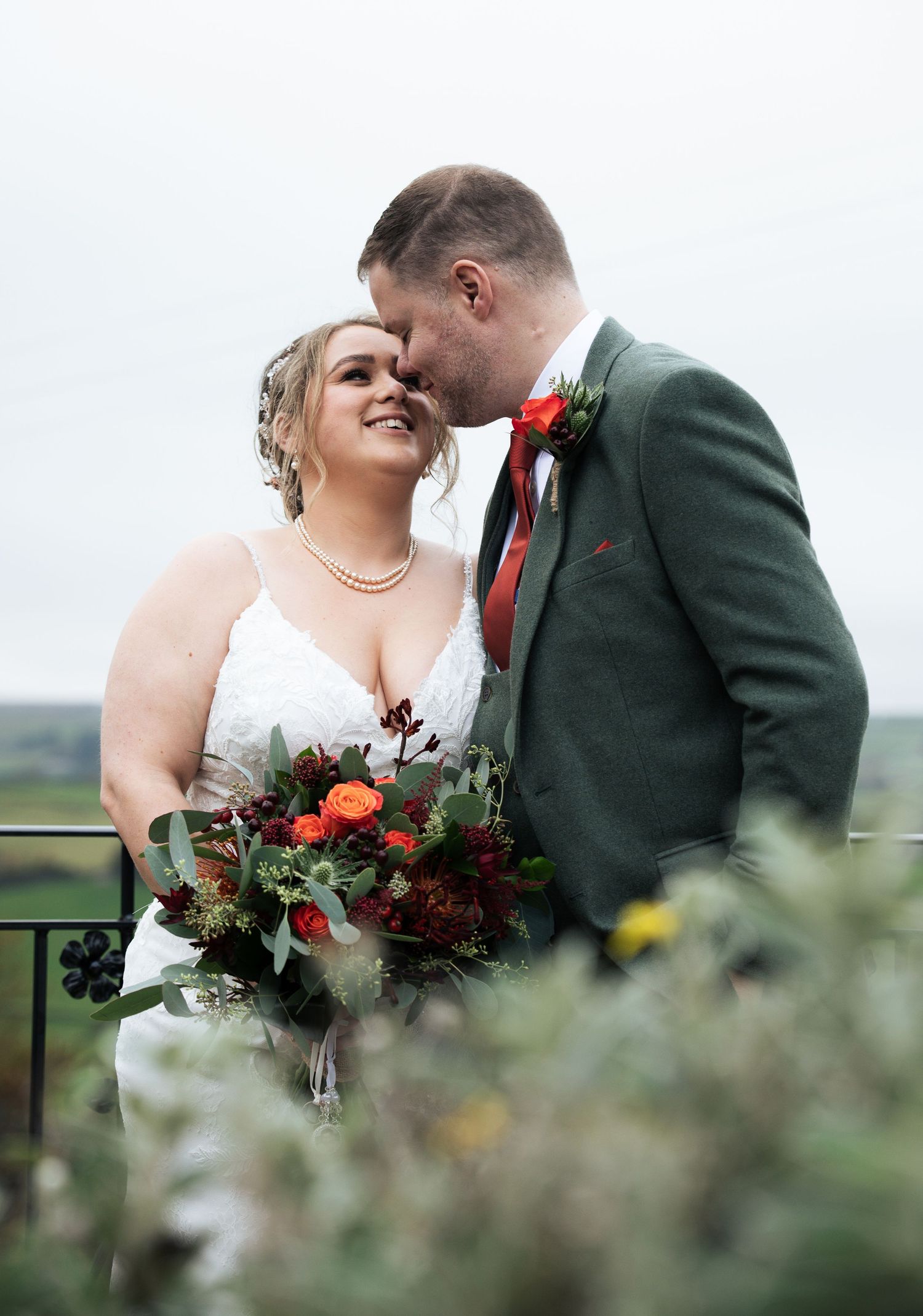 Wedding couple posing with autumn floral bouquet against scenic countryside backdrop, at The Fleece Inn, Halifax.