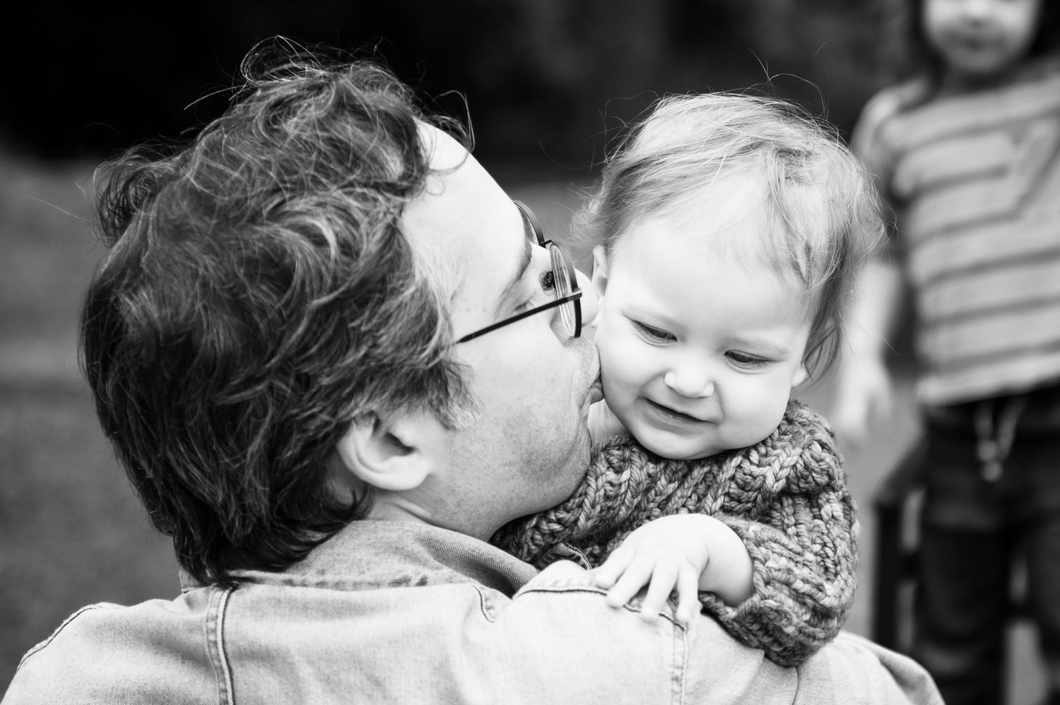 Black and white family photo portrait showing a tender moment of a father kissing his daughter's cheek.