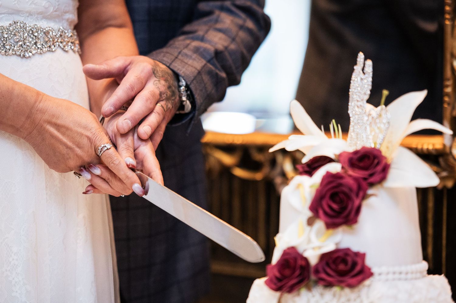 Bride and groom cutting a white wedding cake decorated with red roses and white lilies at their wedding reception.