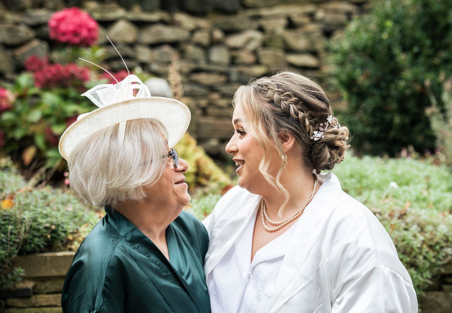 A mother of the bride and bride share a moment together in a garden setting with stone walls, before marriage at The Fleece Inn, Halifax.