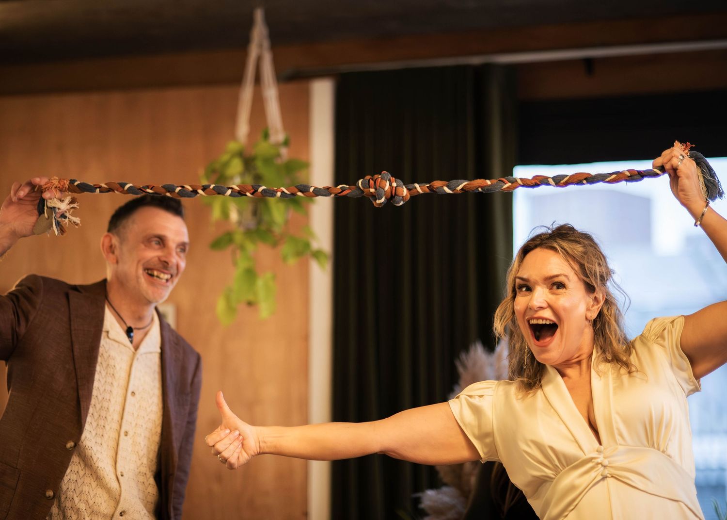 Excited couple pulls apart a braided cord during a fun wedding handfasting ceremony indoors.