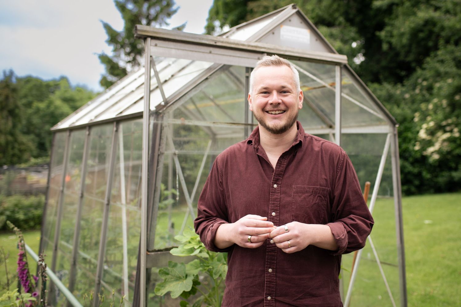 A gardener standing in front of greenhouse in garden setting for his business photos.