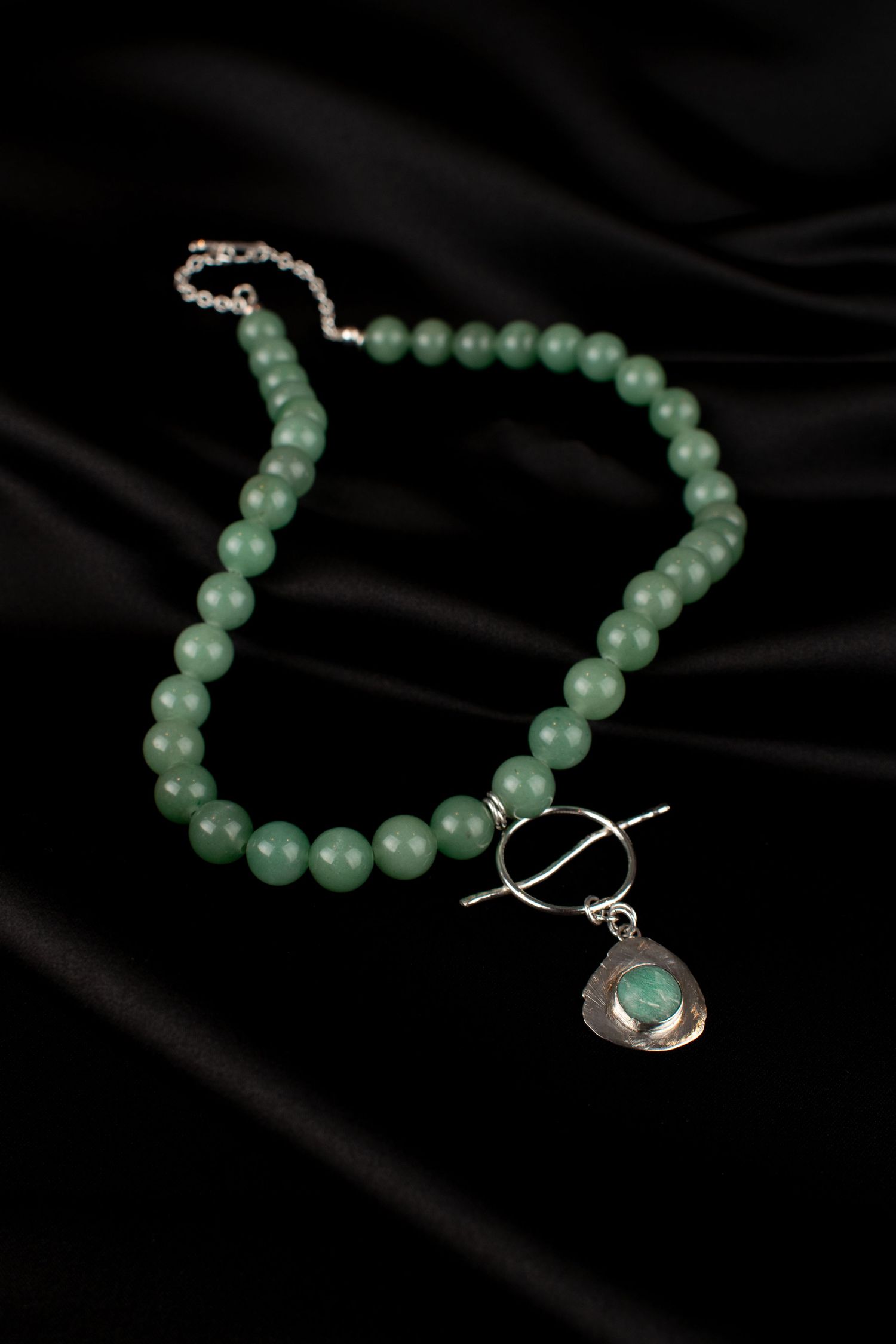 A product shot of a jade green beaded necklace with silver clasp displayed on black silk fabric, for a Leeds jeweller.