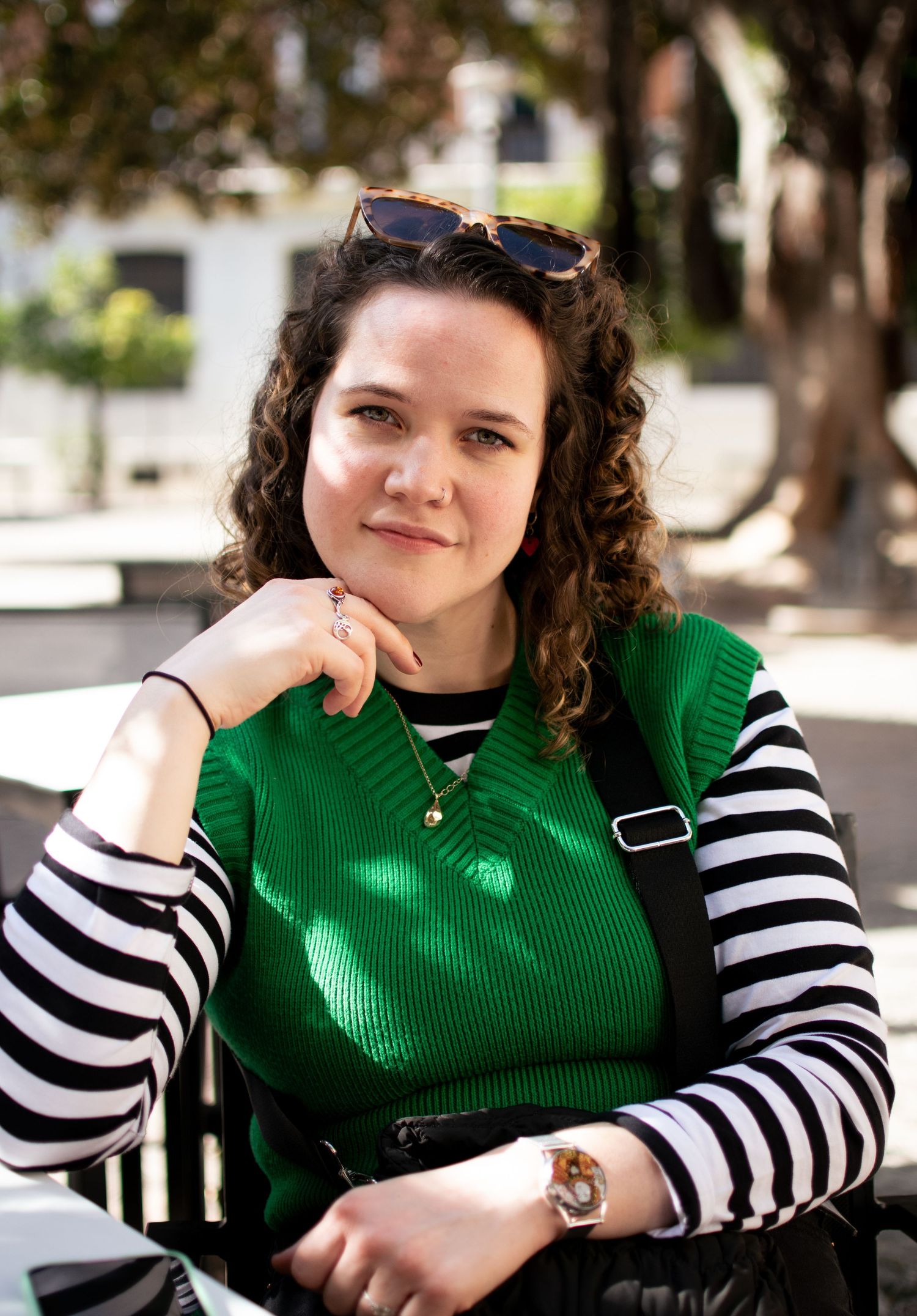 A person wearing a bright green top and striped sleeves poses casually outdoors in a headshot.