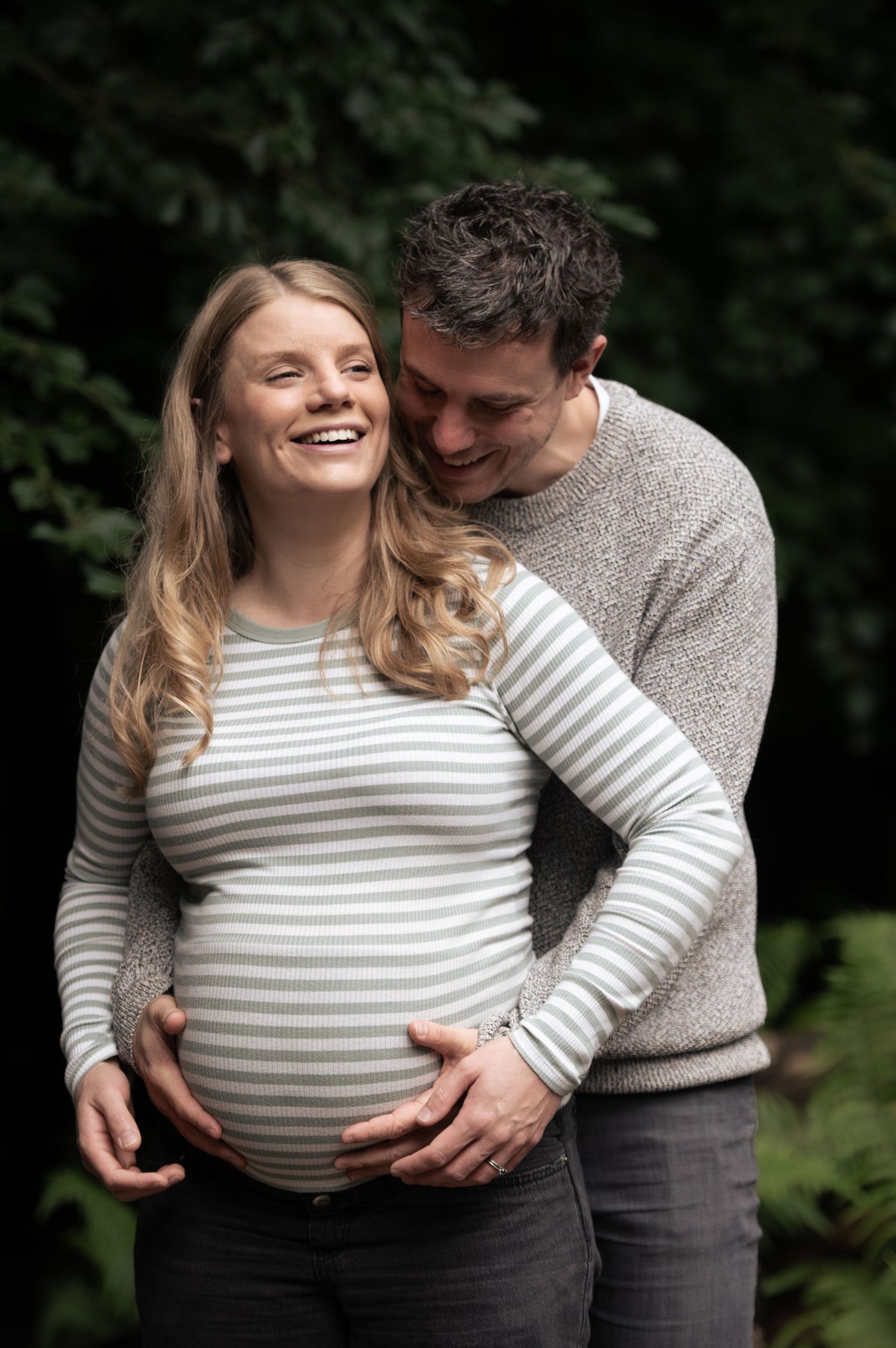 A couple laugh while embracing during their maternity shoot.