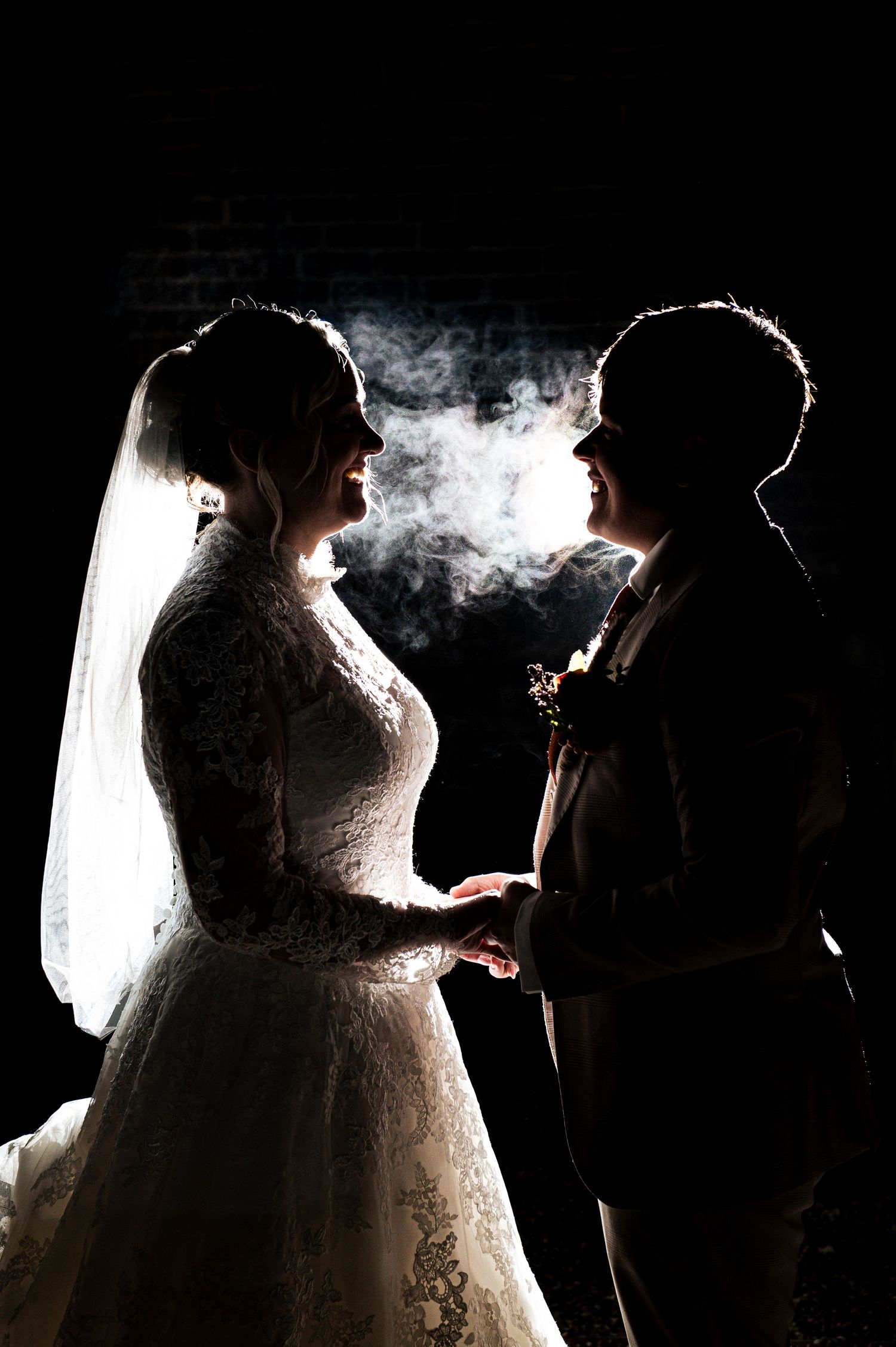 Dramatic backlit silhouette of couple with smoke effects against dark background, at Lodge Farm Weddings, Yorkshire.