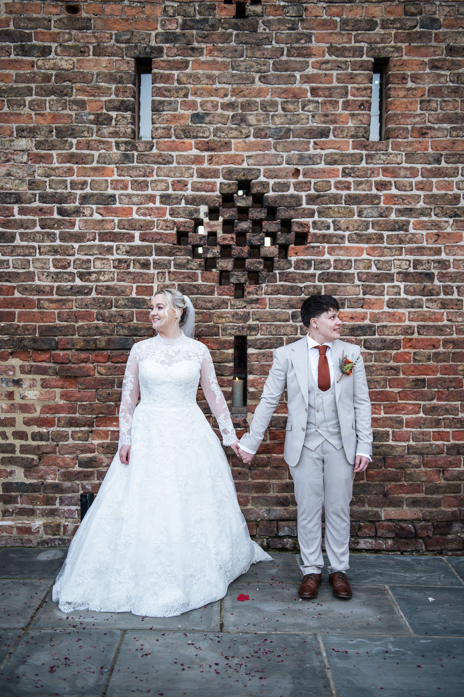 Wedding couple posing playfully against rustic brick wall in formal attire at Lodge Farm Weddings, Yorkshire.