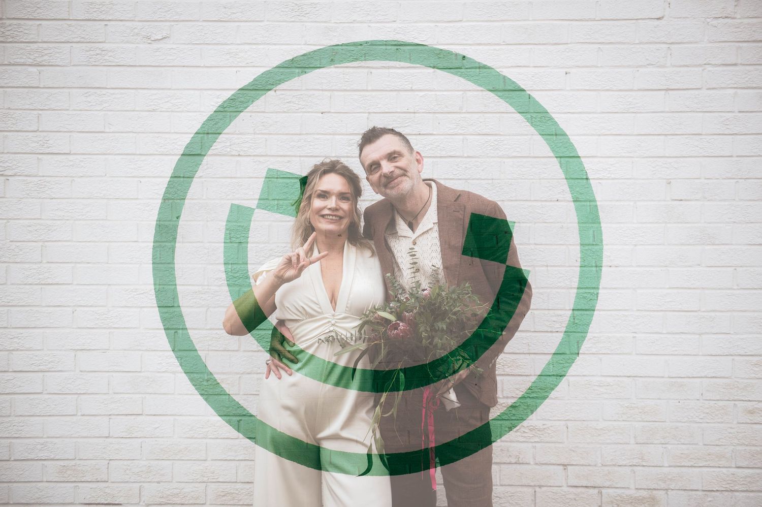 A couple poses together smiling in front of a white brick wall with a green circle graphic overlay.
