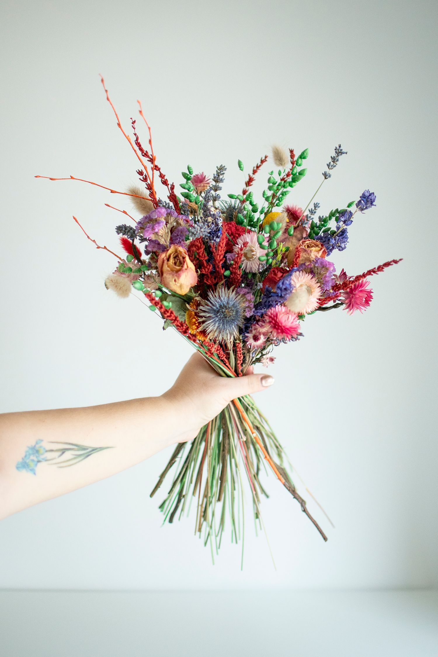 Dried flower bouquet with purple, pink and red blooms held against white background, for a relaxed studio product shot for a Leeds florist.
