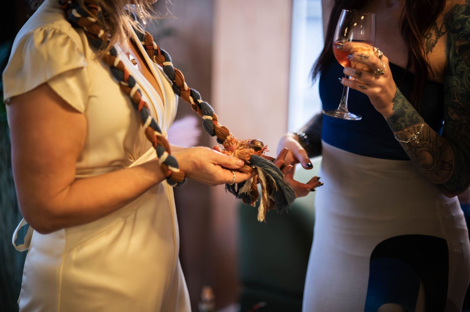 Bride in white dress holding decorative handfasting cord during wedding ceremony ritual.
