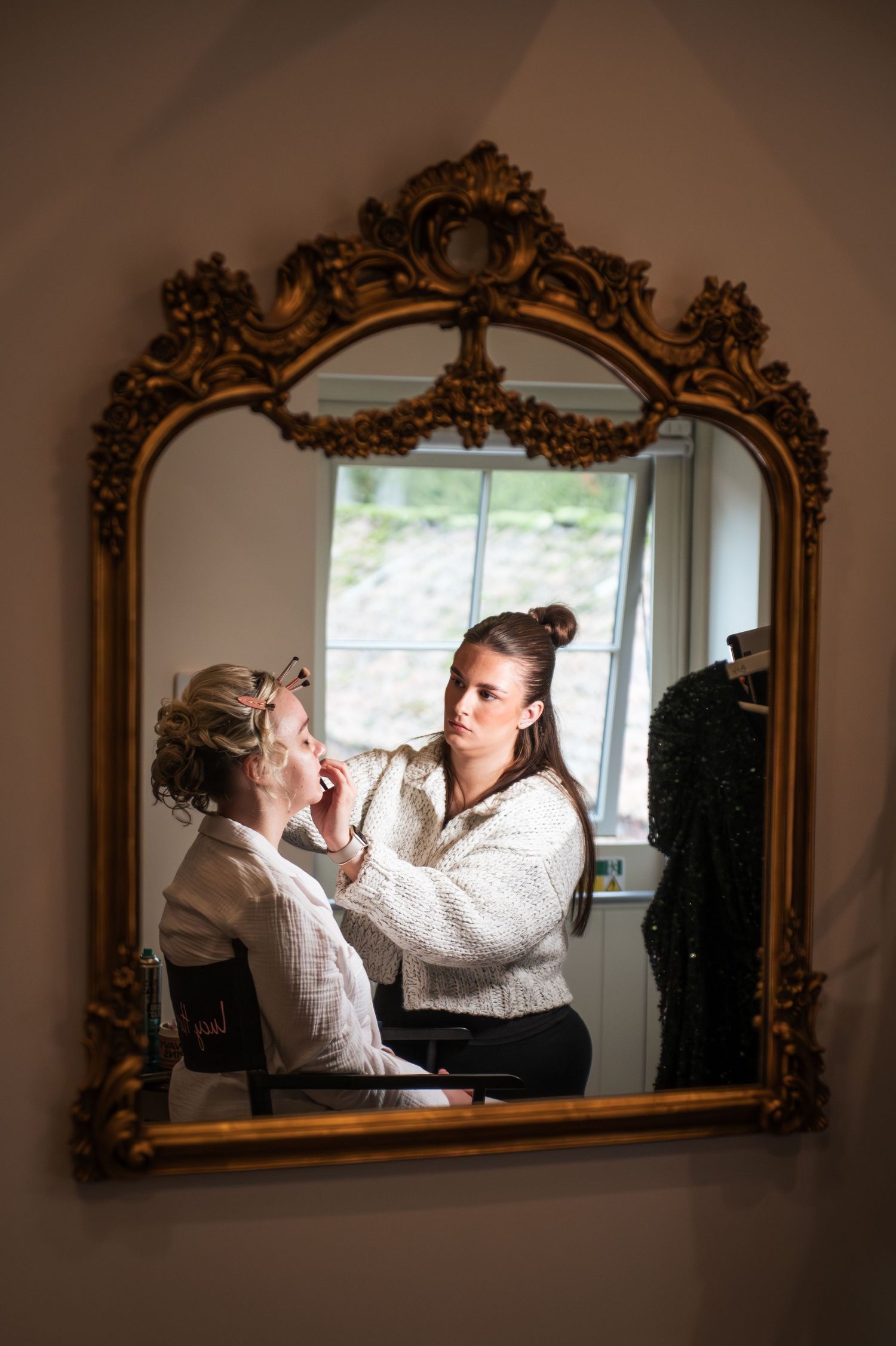 Wedding preparation scene reflected in ornate gold mirror with warm lighting at Lodge Farm Weddings, Yorkshire.