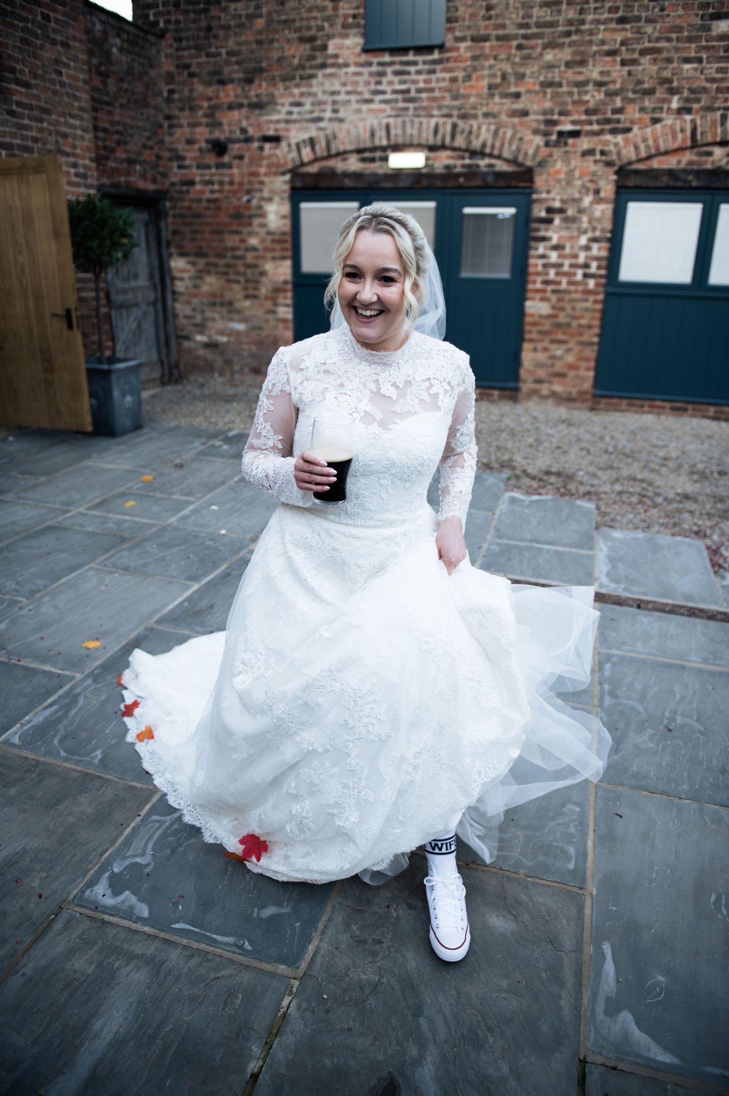 A bride in a white lace dress at her lesbian / LGBT wedding holding a Guiness, at Lodge Farm Weddings, Yorkshire.