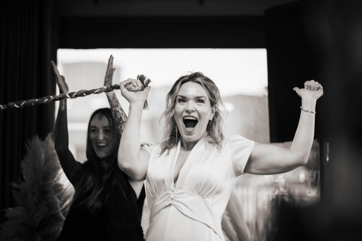 Black and white photo of two women celebrating with arms raised, one holding a rope, both laughing joyfully.