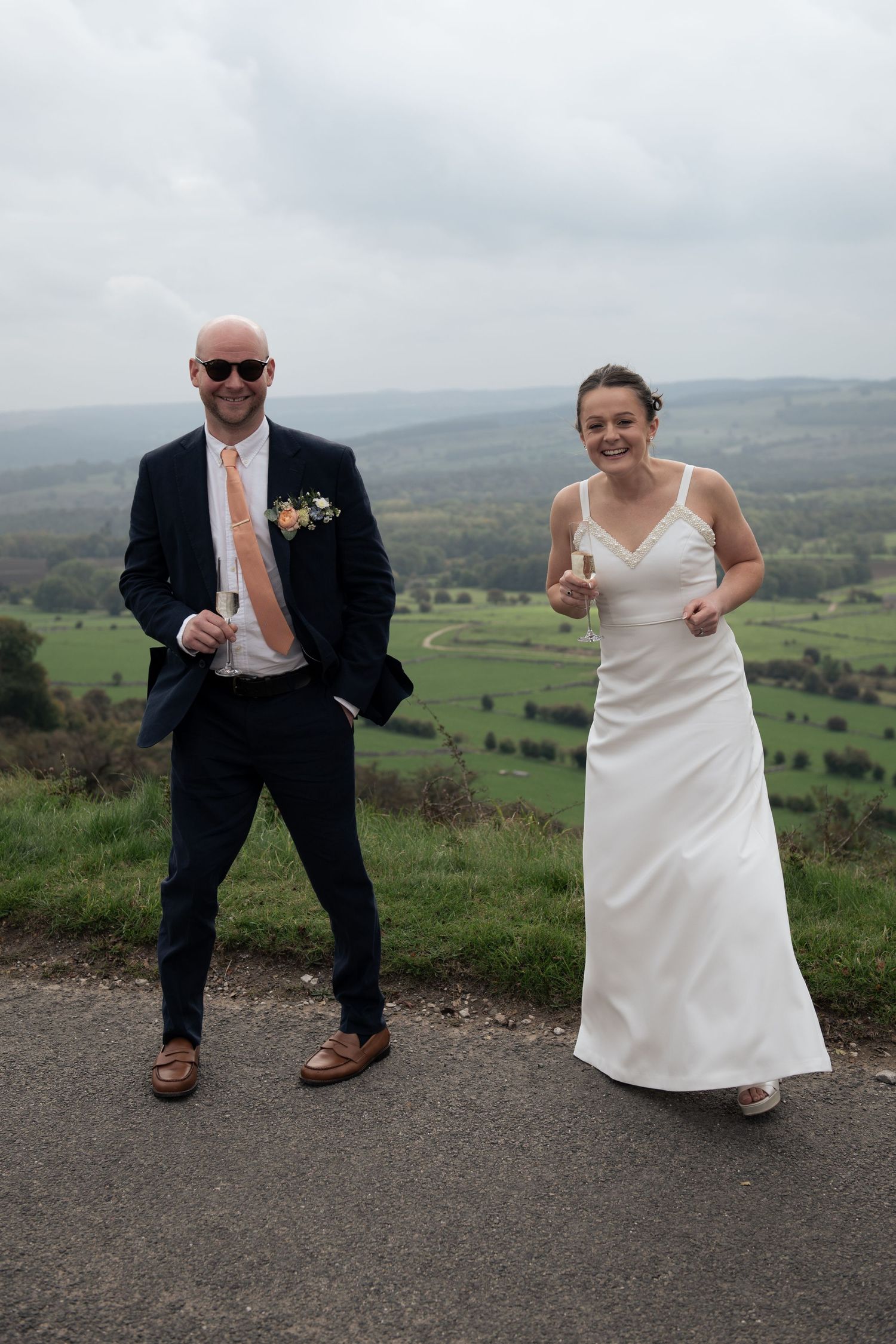 Bride and Groom poses playfully on hilltop with scenic countryside views on Longley Edge, Buxton.