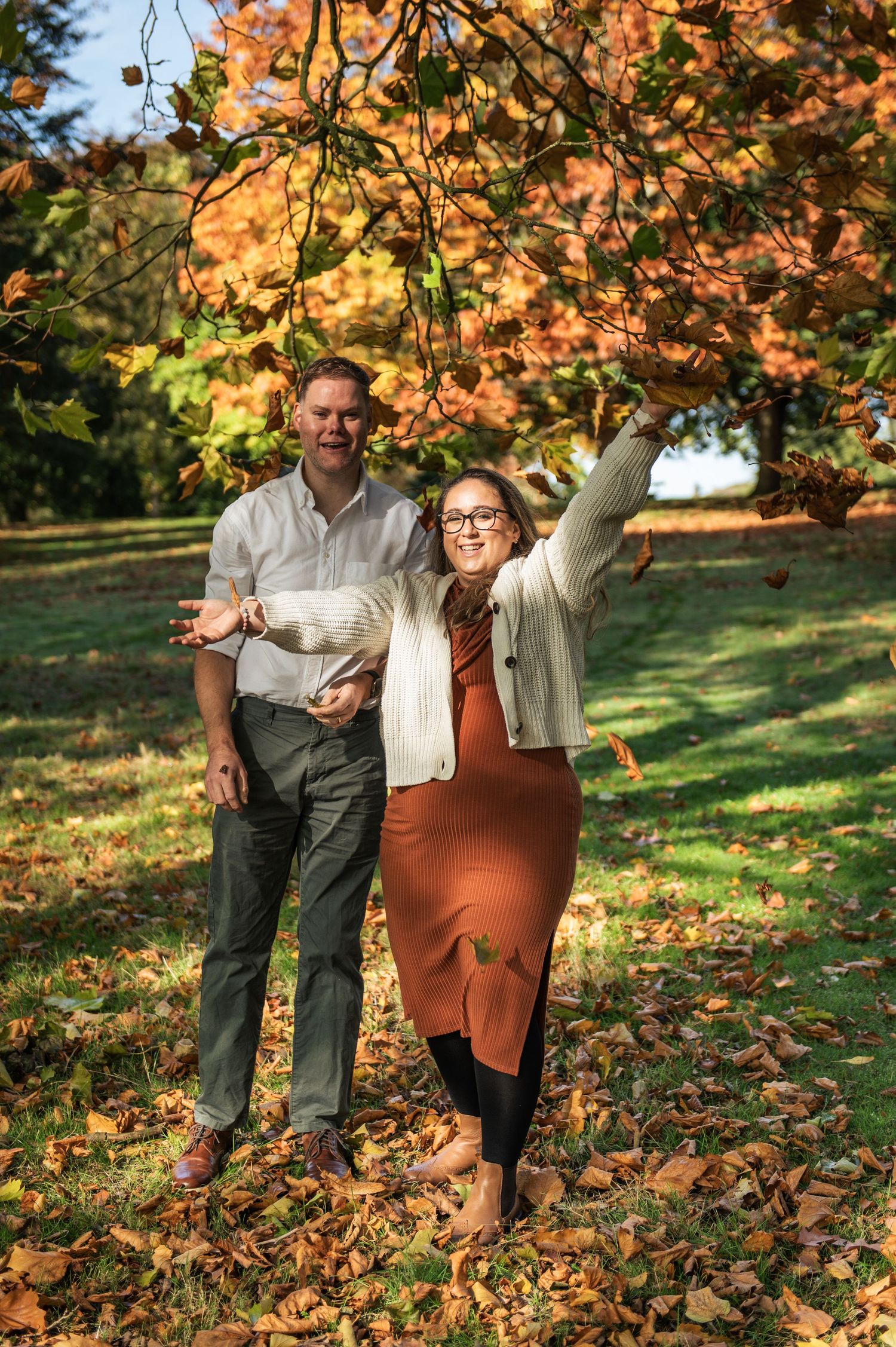 A couple playing with autumn leaves during a fun pregnancy reveal photoshoot in Roundhay Park, Leeds.
