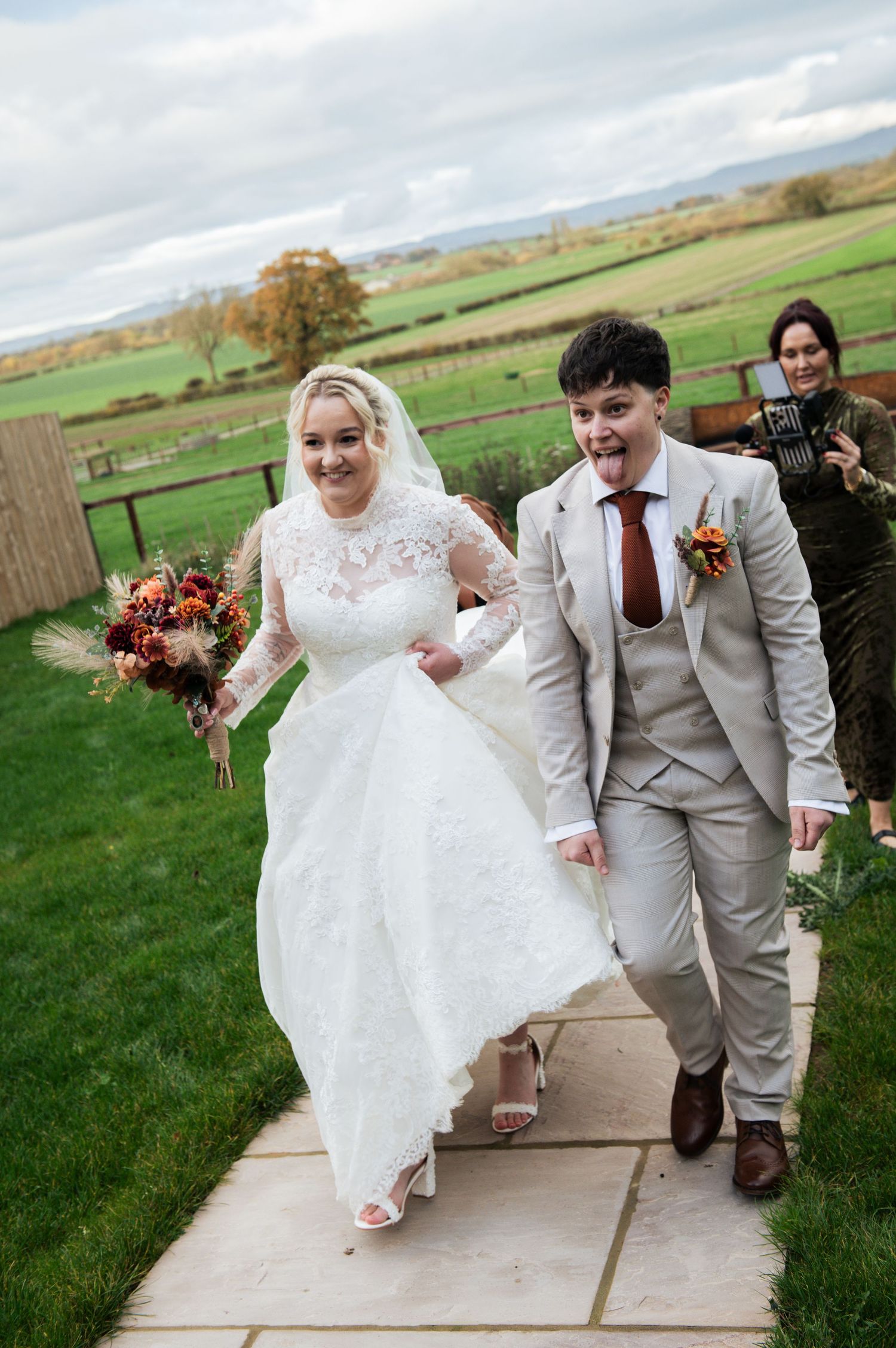Wedding couple walking and laughing together on outdoor path in grey suit and white dress, at Lodge Farm Weddings, Yorkshire.
