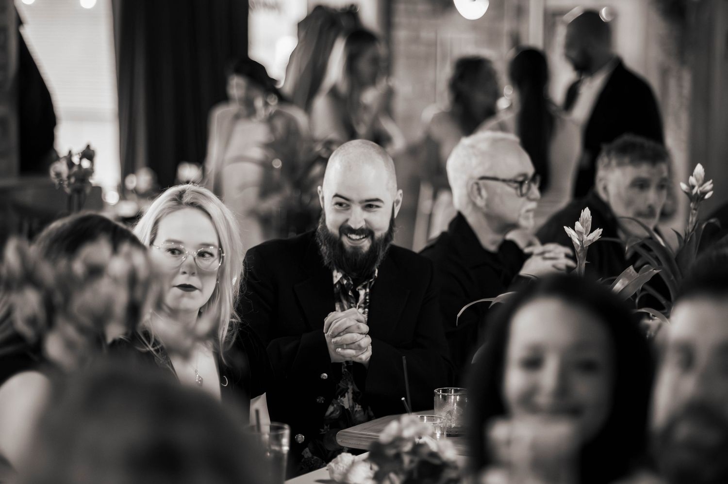 Guests laughing and celebrating at a wedding reception dinner, captured in black and white photography.