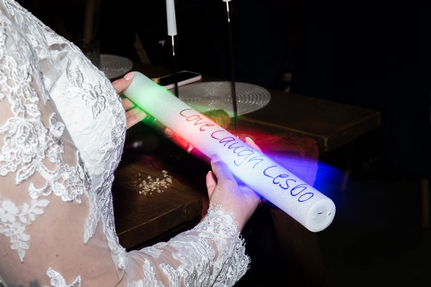 Colourful glow sticks with cheeky lesbian / LGBT jokes illuminate a dark celebration setting, at Lodge Farm Weddings, Yorkshire.